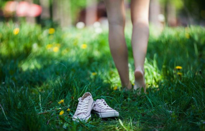 Woman walking barefoot on the grass, pink shoes in focus, shallow DOF